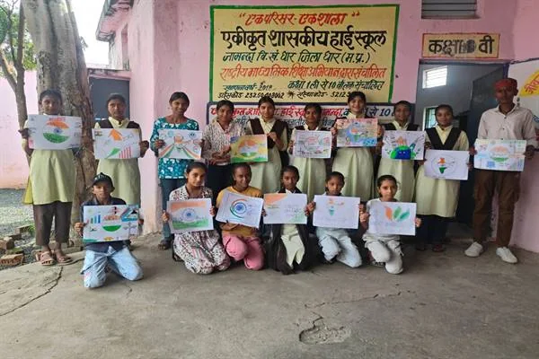 विद्यालय परिसर में छात्र-छात्राएं अपने बनाए रंगीन चित्र हाथों में लेकर समूह में खड़े और बैठे हैं