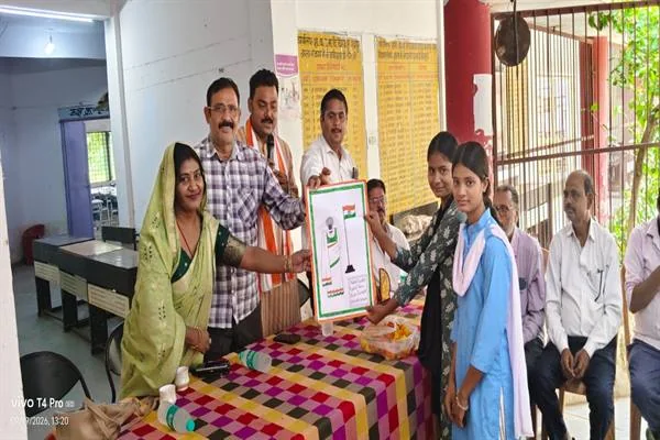 विद्यालय के कक्ष में एक छात्रा को चित्रकला की फ्रेम की हुई कृति देते अतिथि, पास खड़े शिक्षक और अन्य लोग