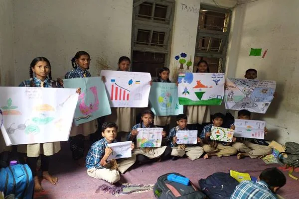 विद्यालय की वर्दी पहने बच्चे कमरे में अपने बनाए रंगीन चित्र हाथों में लेकर बैठे और खड़े हैं