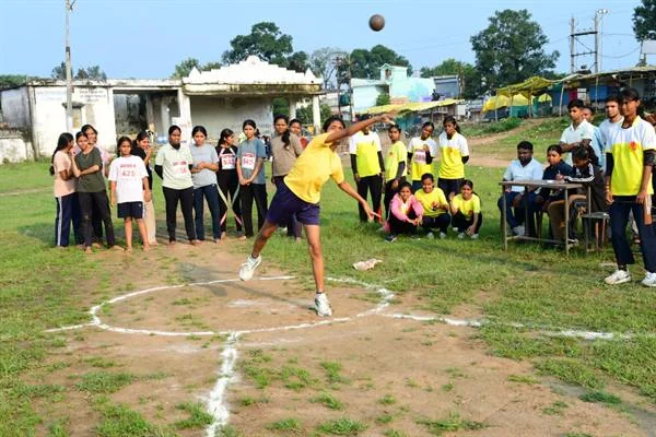 खुले खेल मैदान में गोला फेंकती युवती और आसपास खड़े प्रतिभागी व अधिकारी
