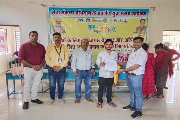 हॉल में 'सेवा संकल्प अभियान के अंतर्गत, युवा संगम कार्यक्रम' लिखे बैनर के सामने खड़े पांच लोग, जिनमें से एक अधिकारी युवक को कागज सौंप रहा है।